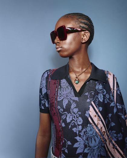 Model in a floral-patterned Etro polo shirt, accessorized with oversized sunglasses and a statement necklace.