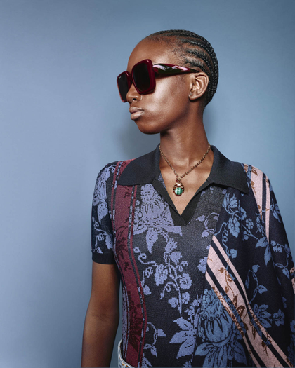 Model in a floral-patterned Etro polo shirt, accessorized with oversized sunglasses and a statement necklace.