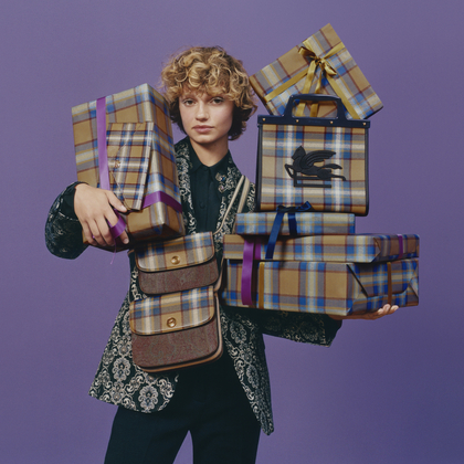 Gift Guide for him and her. Picture of girl in Paisley suit jacket, holding reglo packets with Check paper in his arms, paired with ETRO Clutch Bag, Essential Handbags and Love Trotter Bags in tartan print.