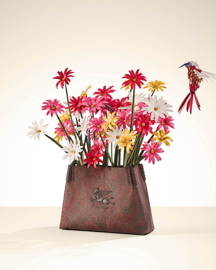 A Libra Etro bag filled with colorful daisy flowers and a small, detailed bird hovering nearby