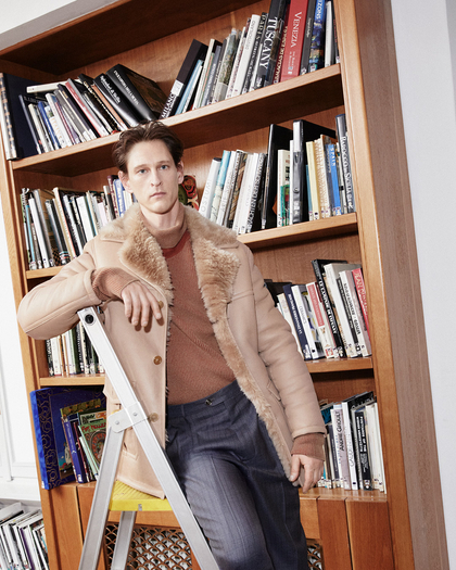 Model wearing a camel SHEARLING COAT in front of a library