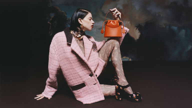 girl-sitting-in-a-pink-check-wool-jacket-polka-dot-and-Paisley-tights-and-embroidered-Mary-Jane-shoes-carries-an-orange-Satuno-bag.