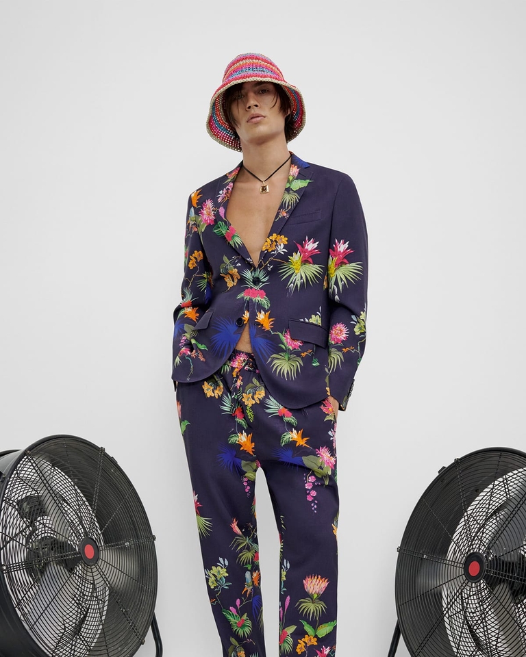Young man standing up wearing floral and leafy print suit and striped tricot hat - SS23 man collection