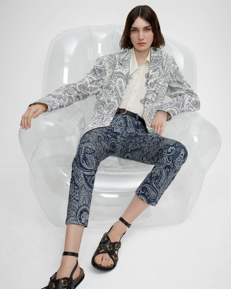 테일러드 재킷, Paisley 패턴 진, Crown Me 샌들을 신고 고무 의자에 앉아 있는 여성 - SS23 여성 컬렉션 