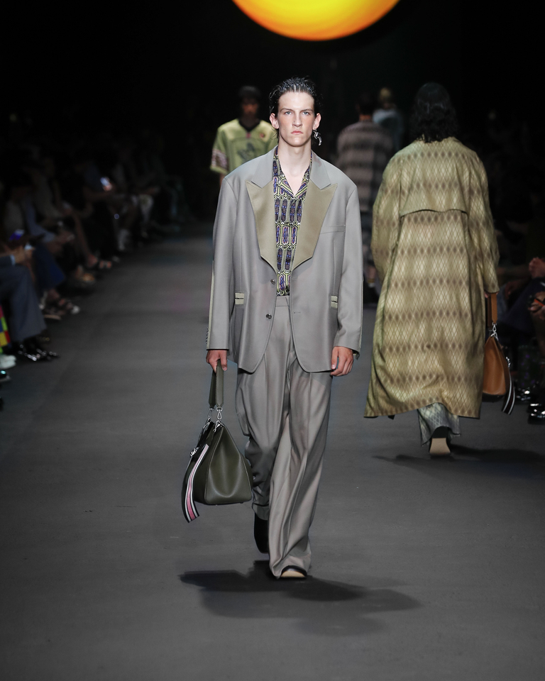 Model with grey elegant suit, multicoloured shirt with geometric patterns and dark green bag from the Etro Spring Summer collection 2024 fashion show