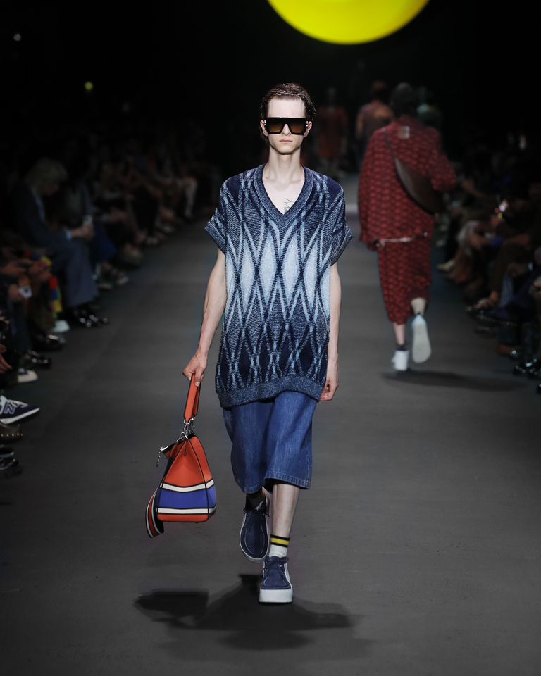 Model with sunglasses, blue and light blue sleeveless jumper, short jeans and orange bag Etro Spring Summer collection 2024 fashion show