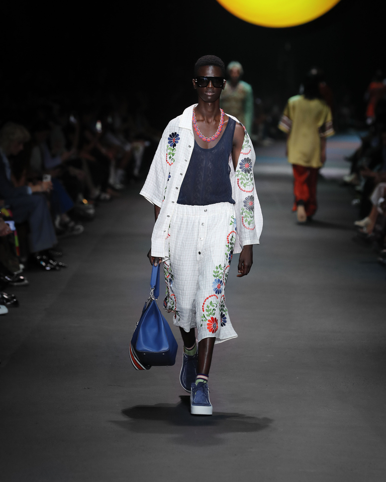 Model with multicoloured necklace, white shirt, white short trousers with floral patterns and blue bag Etro Spring Summer collection 2024 fashion show