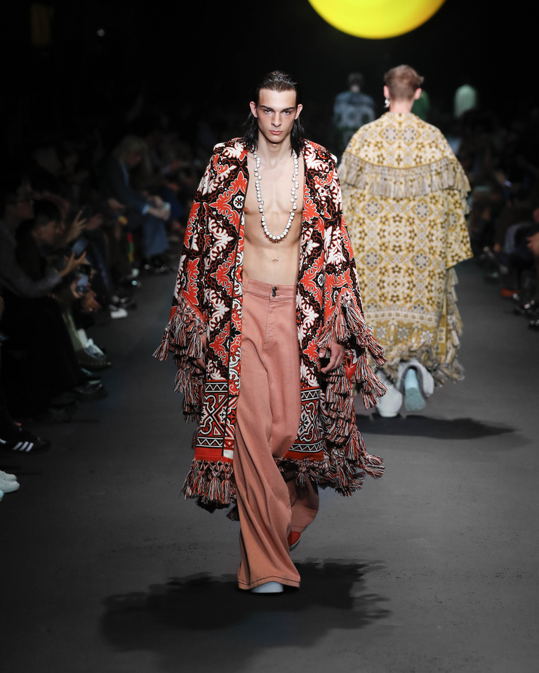 Model wearing a white necklace, orange poncho and orange long trousers from the Etro Spring Summer collection 2024 fashion show